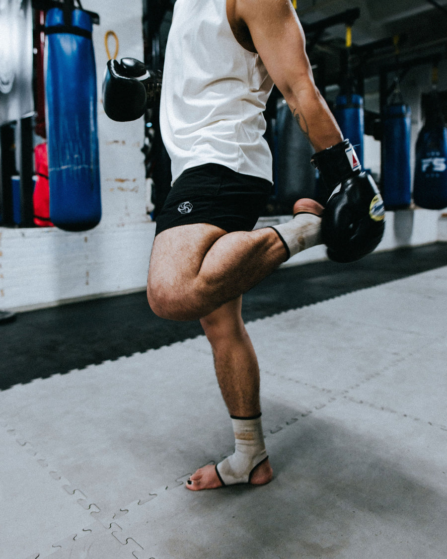 A man stretches his quad muscles in a white tee and black shorts.
