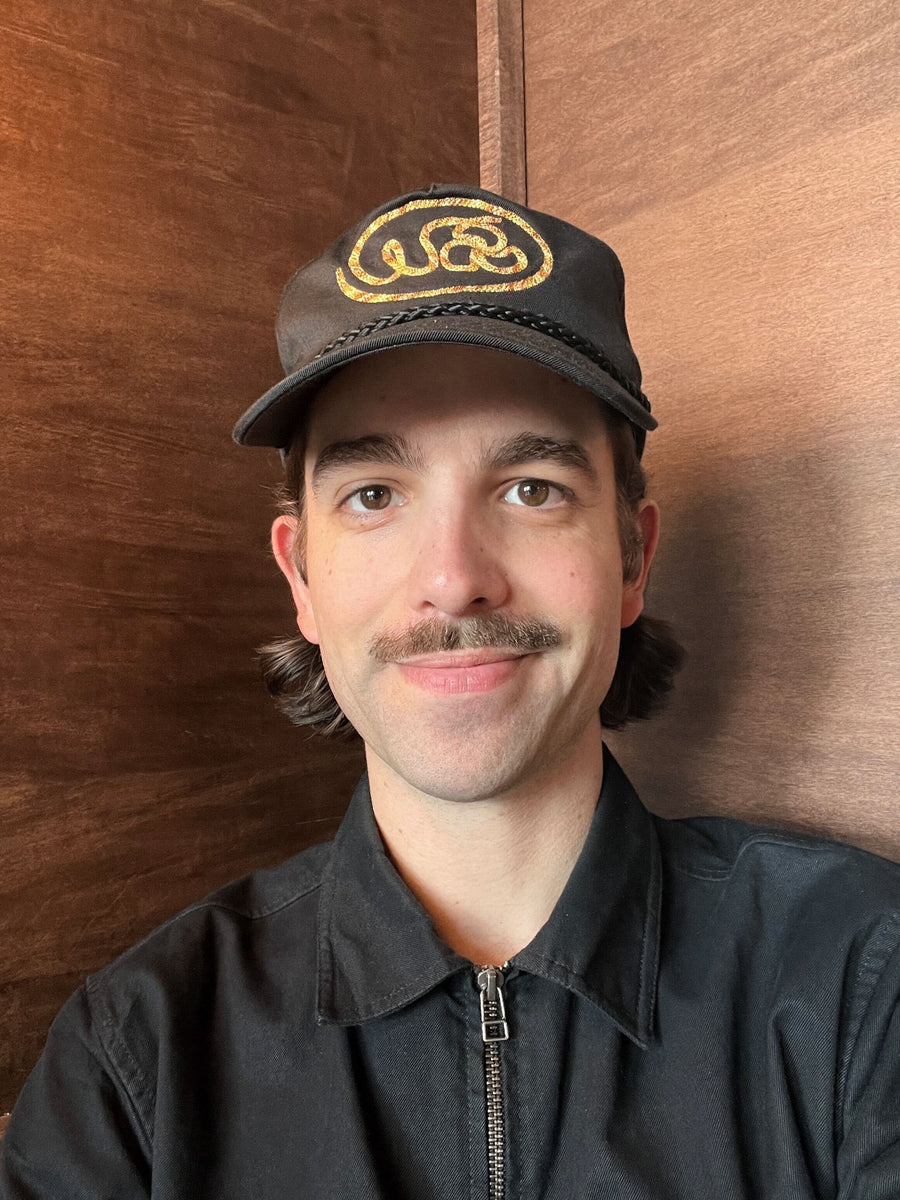 A man in a black hat smiles and looks into the camera.