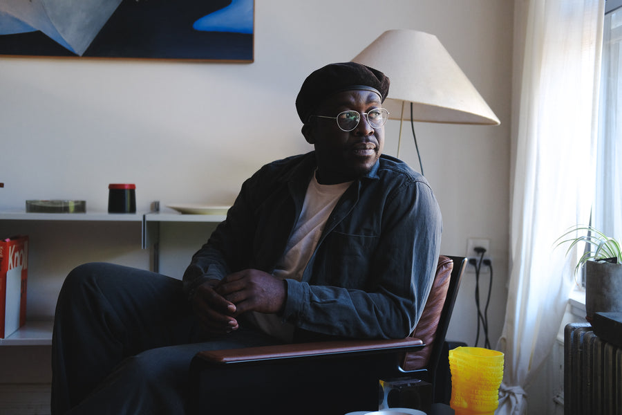 A handsome man sits in his well-designed apartment in our smoke garment dyed shop jacket.