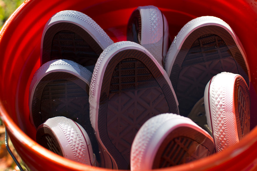 The toes of several Converse sneakers peek out of an orange bucket, soaking in a liquid.