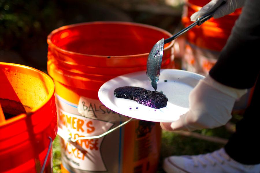 Several orange buckets sit on the ground, holding indigo dye.