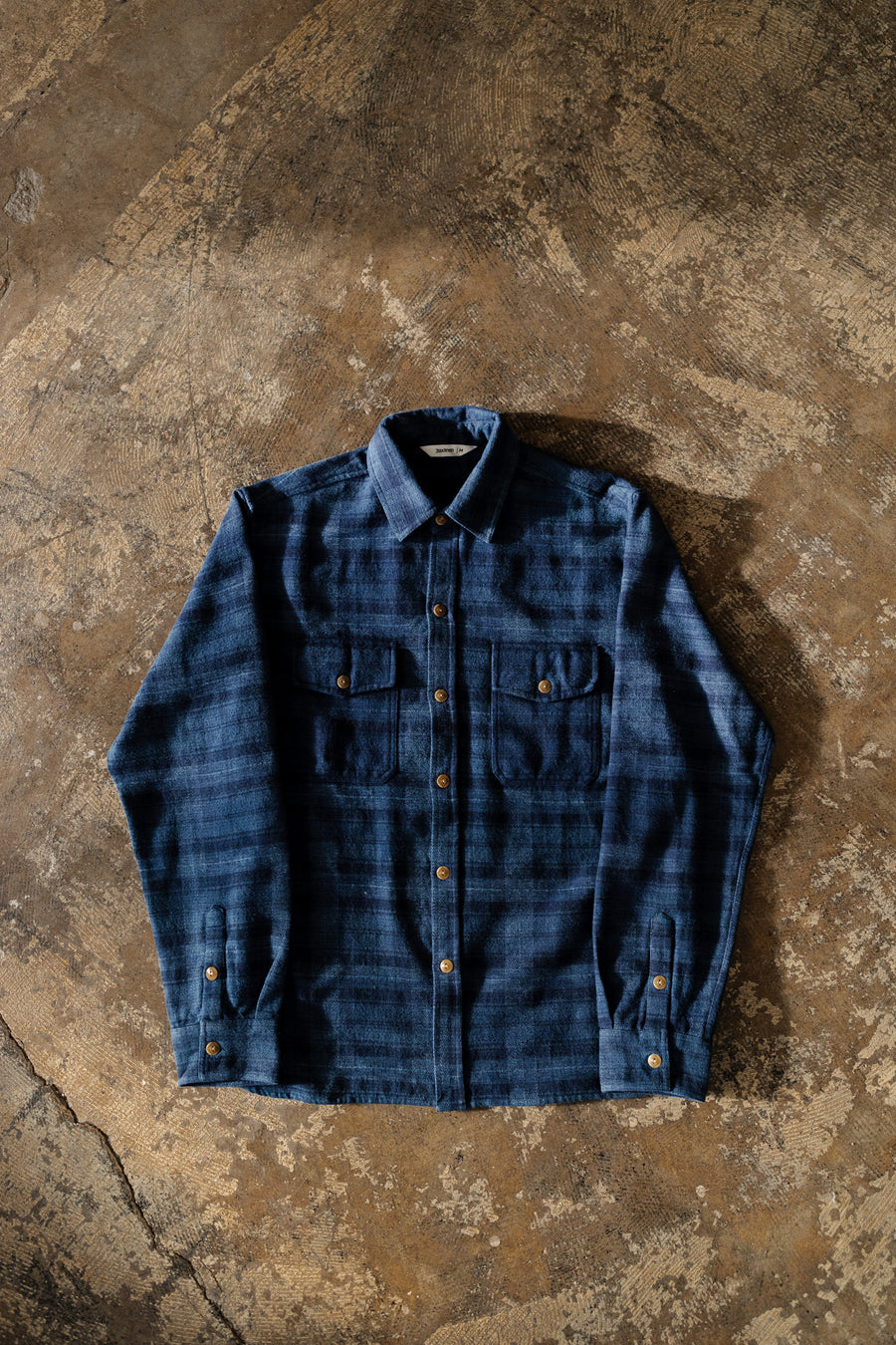 A blue flannel lying flat on a concrete floor.