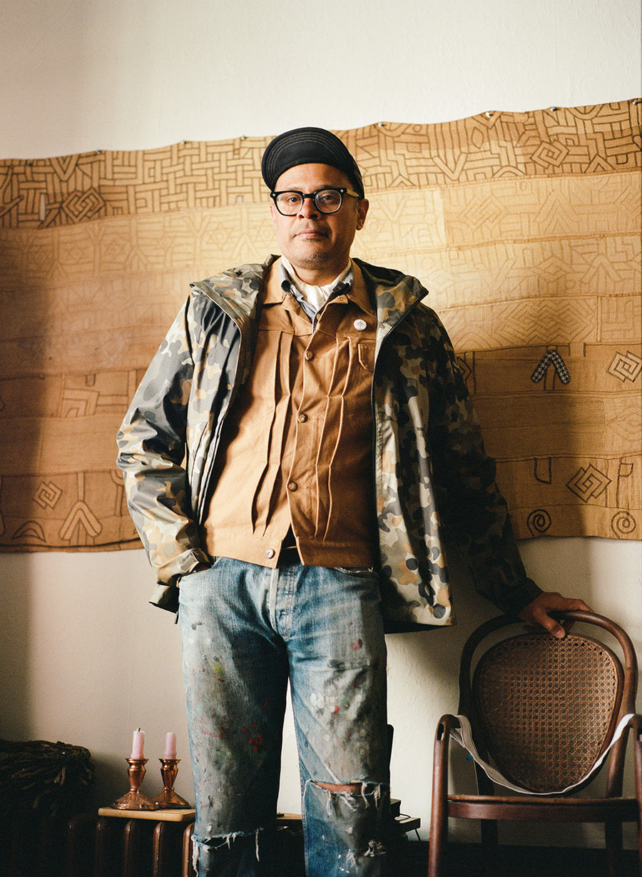 A man stands in a room with a tapestry hanging on a wall.
