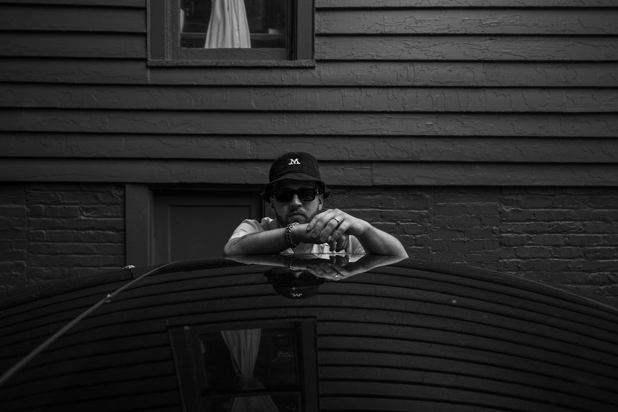 A black & white photo of a man standing behind a car.