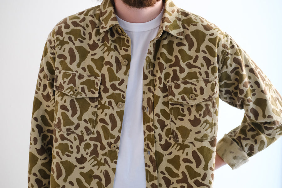 A man wears a camouflage shirt against a white background.