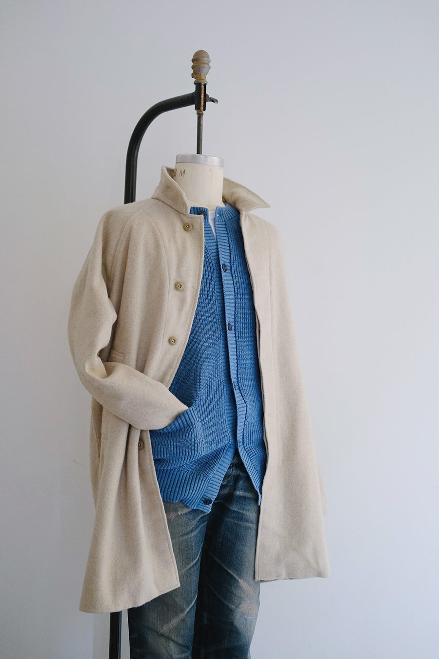 A mannequin with a coat and a blue sweater on it.