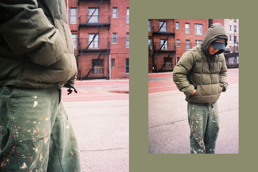 A young man wears the down jacket with paint splattered fatigues.