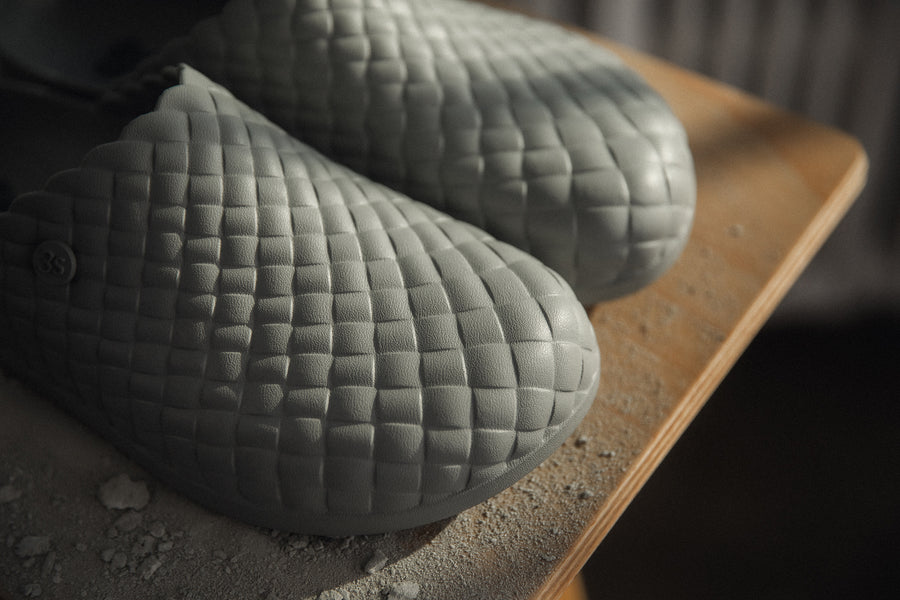 A close up image of a woven pattern on a pair of grey clogs.