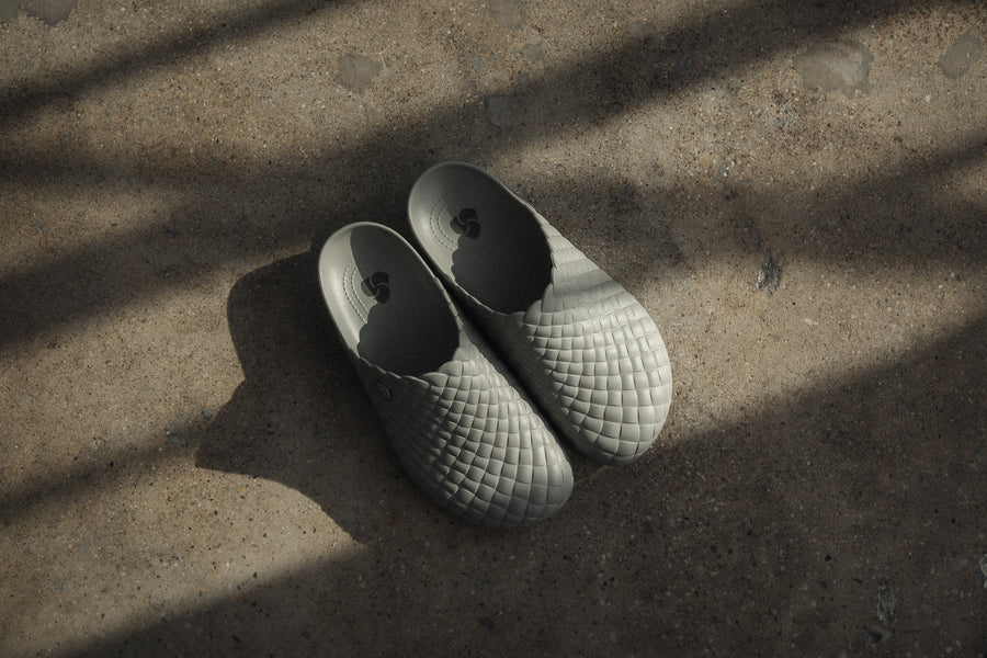 A pair of grey Crocs clogs on a stone floor with shadows cast over them.