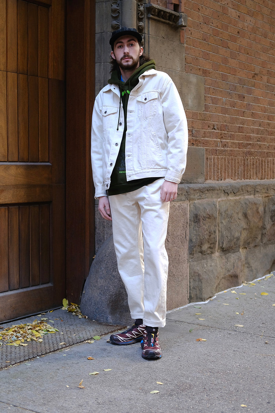 A man in white pants and jacket stands in front of a wooden door.