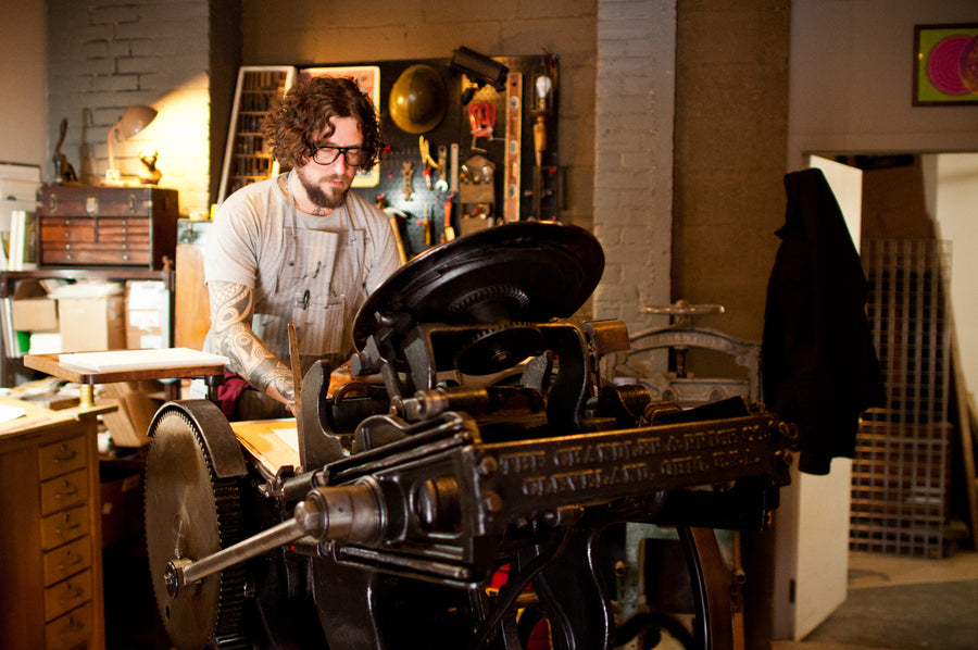 A man is standing up and operating a printing press.