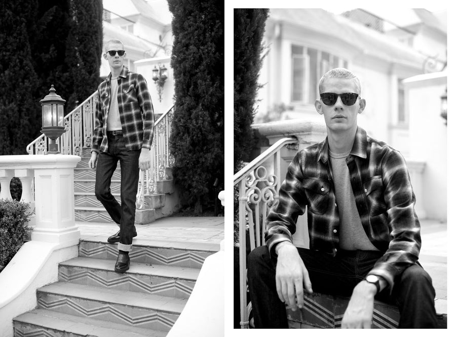 A man stands on stairs wearing sunglasses and a 3sixteen flannel.