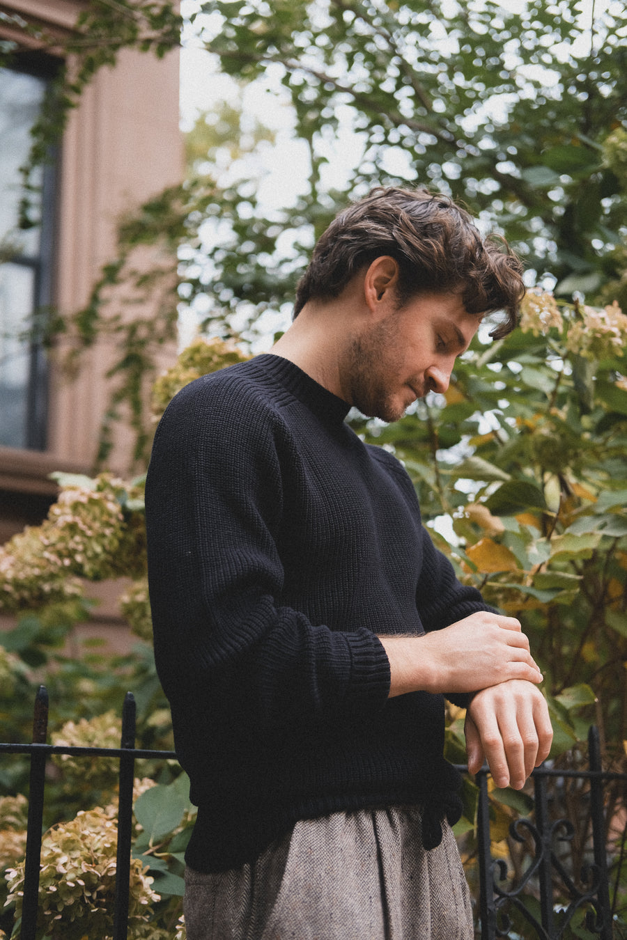 A man in a black sweater looks at his wrist.