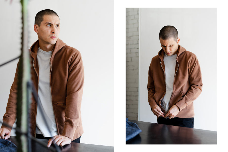 A handsome young man wears the clove zip hoody and looks off into the distance.