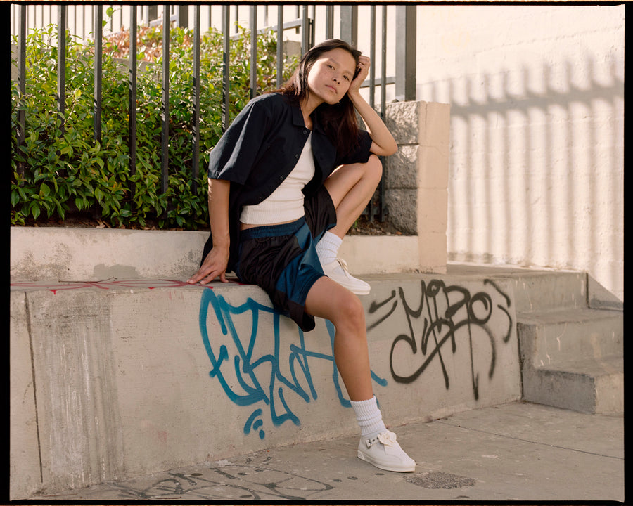 A woman in a navy shirt and mesh shorts sits on a curb.