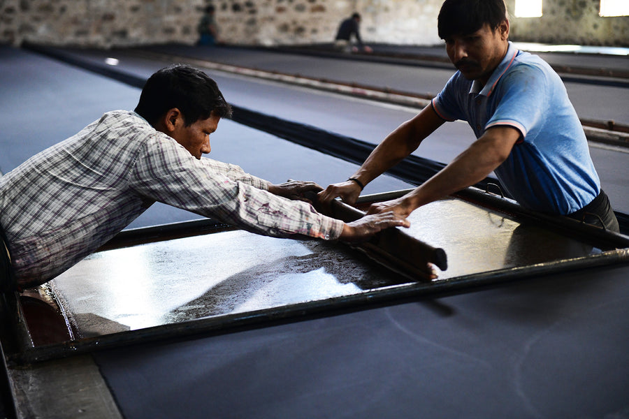 Two men screen print a fabric.