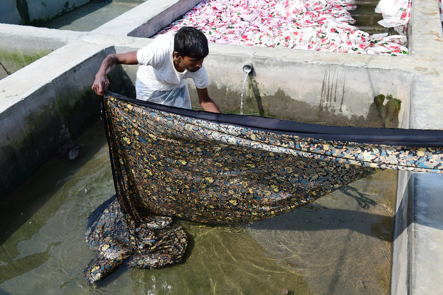 Fabric is washed out in a large concrete basin of water.