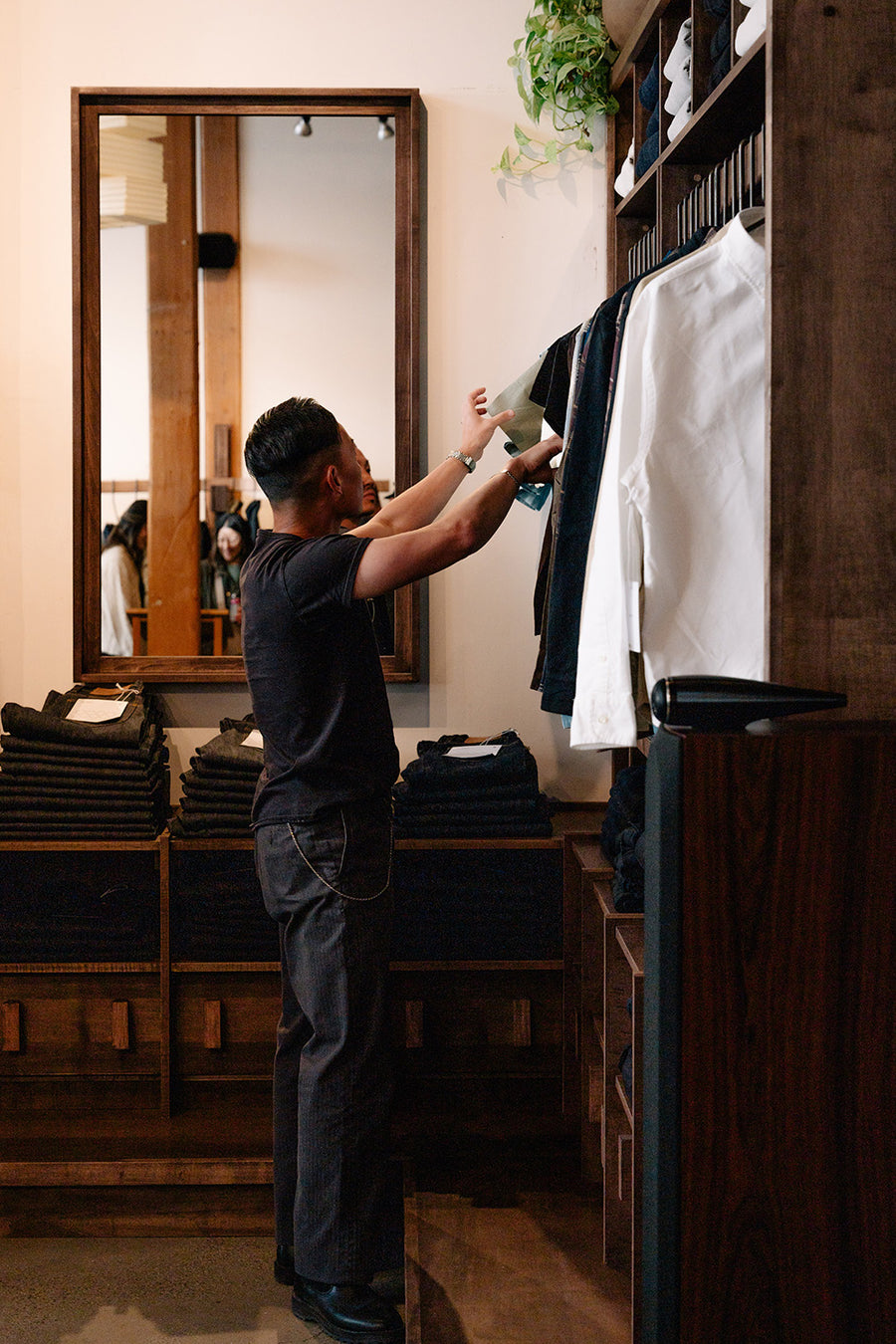 A man looks at clothing hanging on a dark wooden rack.