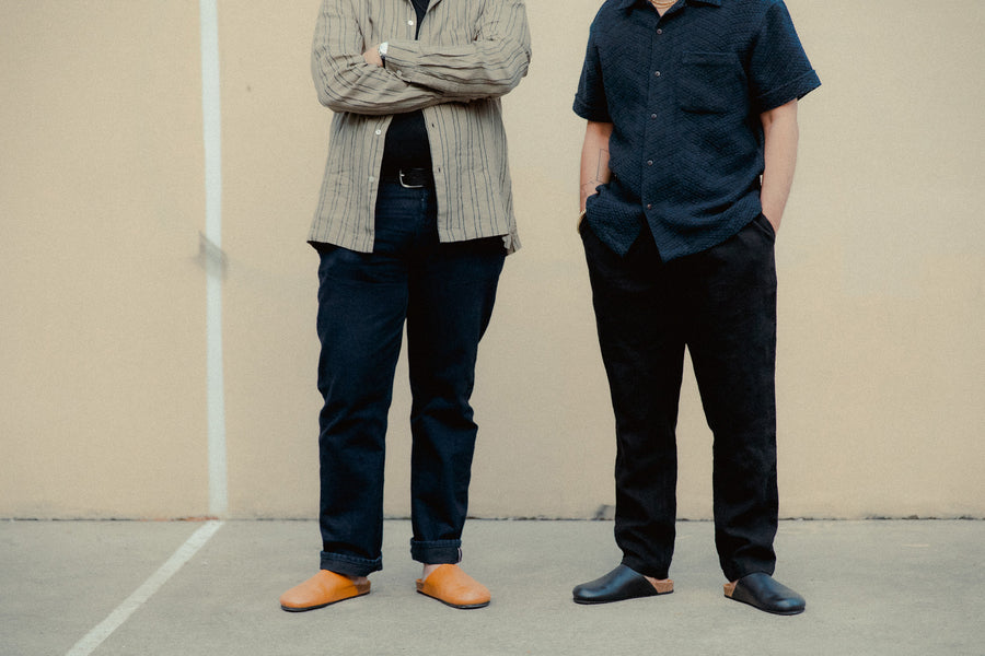 Two men stand on a handball court in tan and black mules.