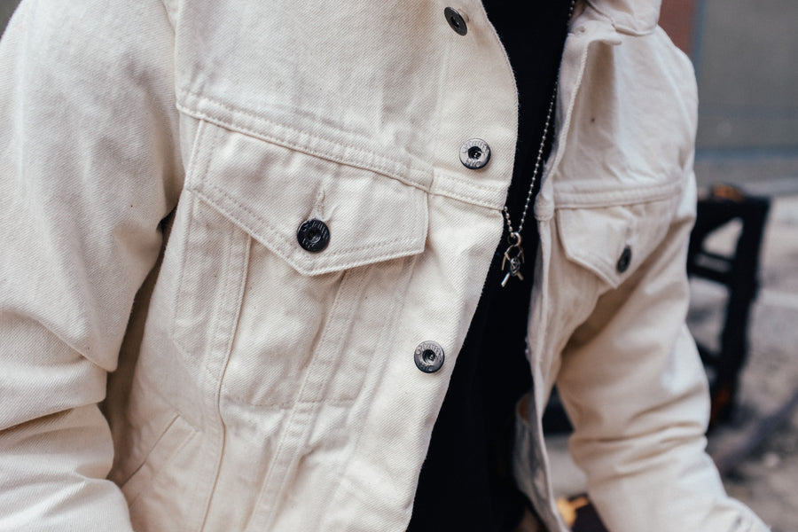 The natural denim jacket is modeled worn over a black tee.