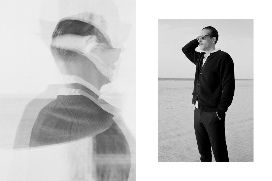 A man in a black cardigan and sunglasses pushes his hair back.