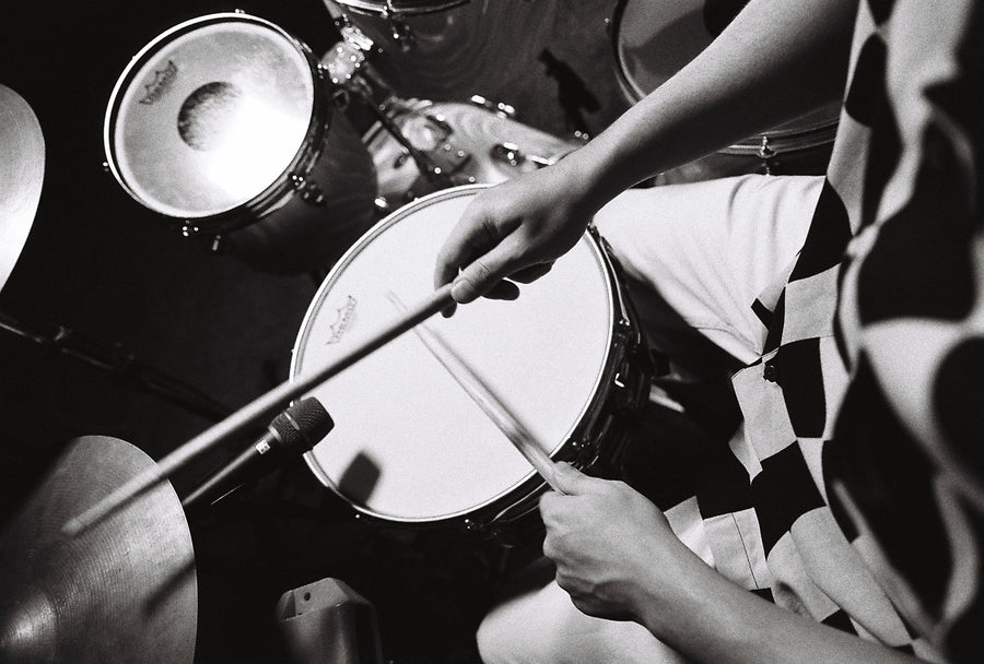 A black and white photo of someone playing drums in a checkered shirt.