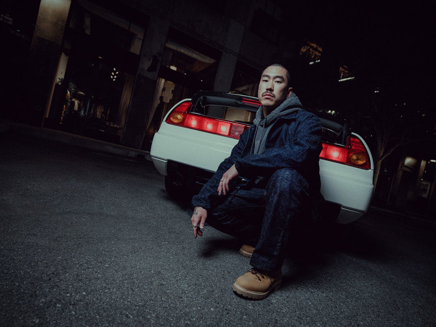 A man crouches next to a Honda NSX-R in a parking lot.