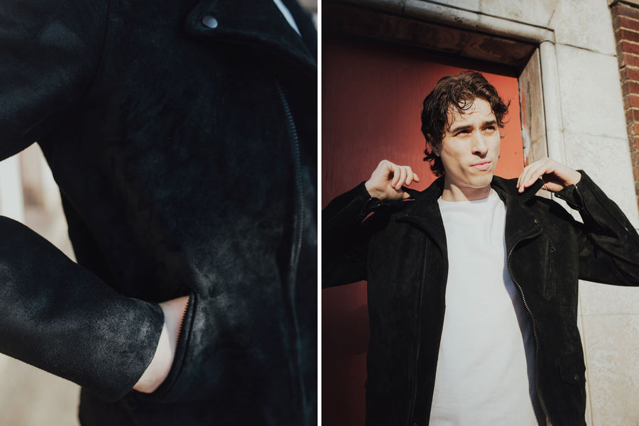 The model puts his hand into the jacket and adjusts its collar.