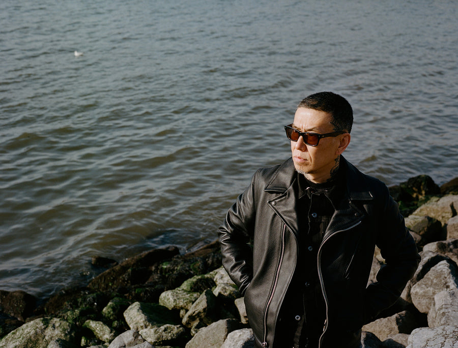 A man wears a leather jacket while looking out onto the waterfront.