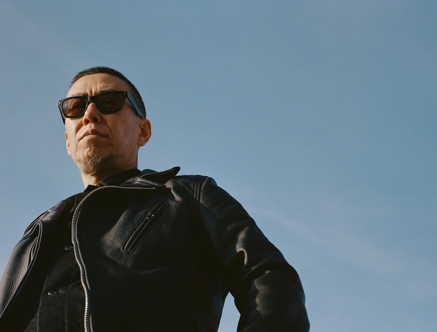 A man wears a black leather jacket against a bright blue sky.