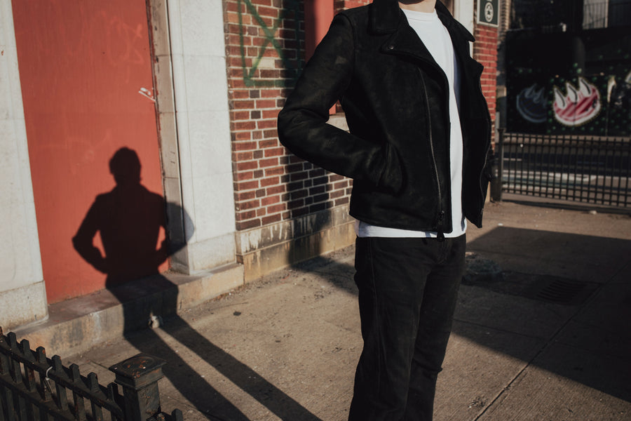 A model wears a black leather jacket while the sun casts a long shadow behind him.