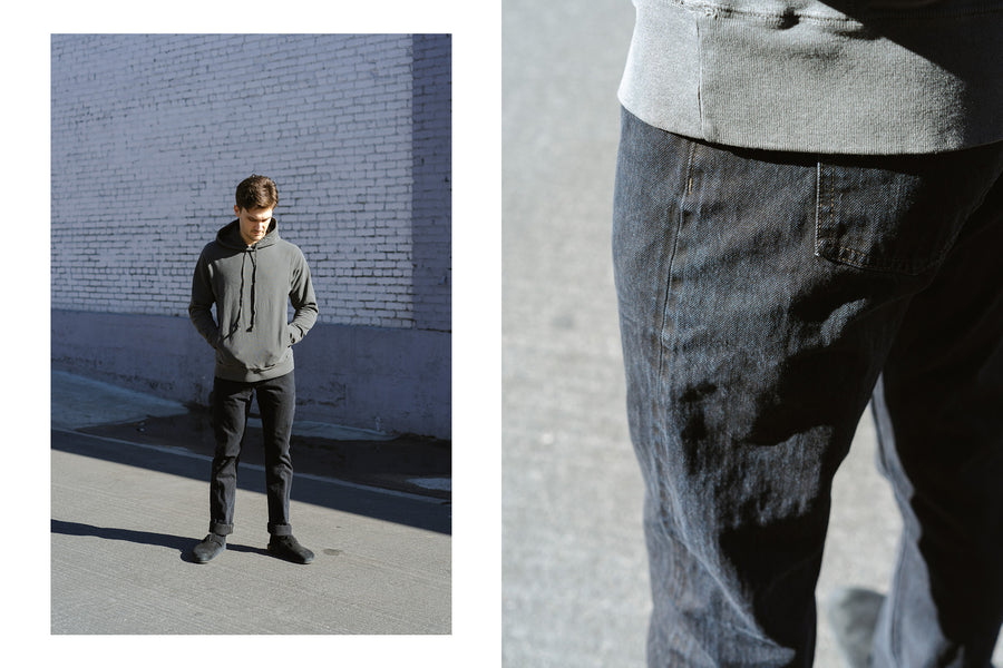 A man wears a grey hoodie and black denim.