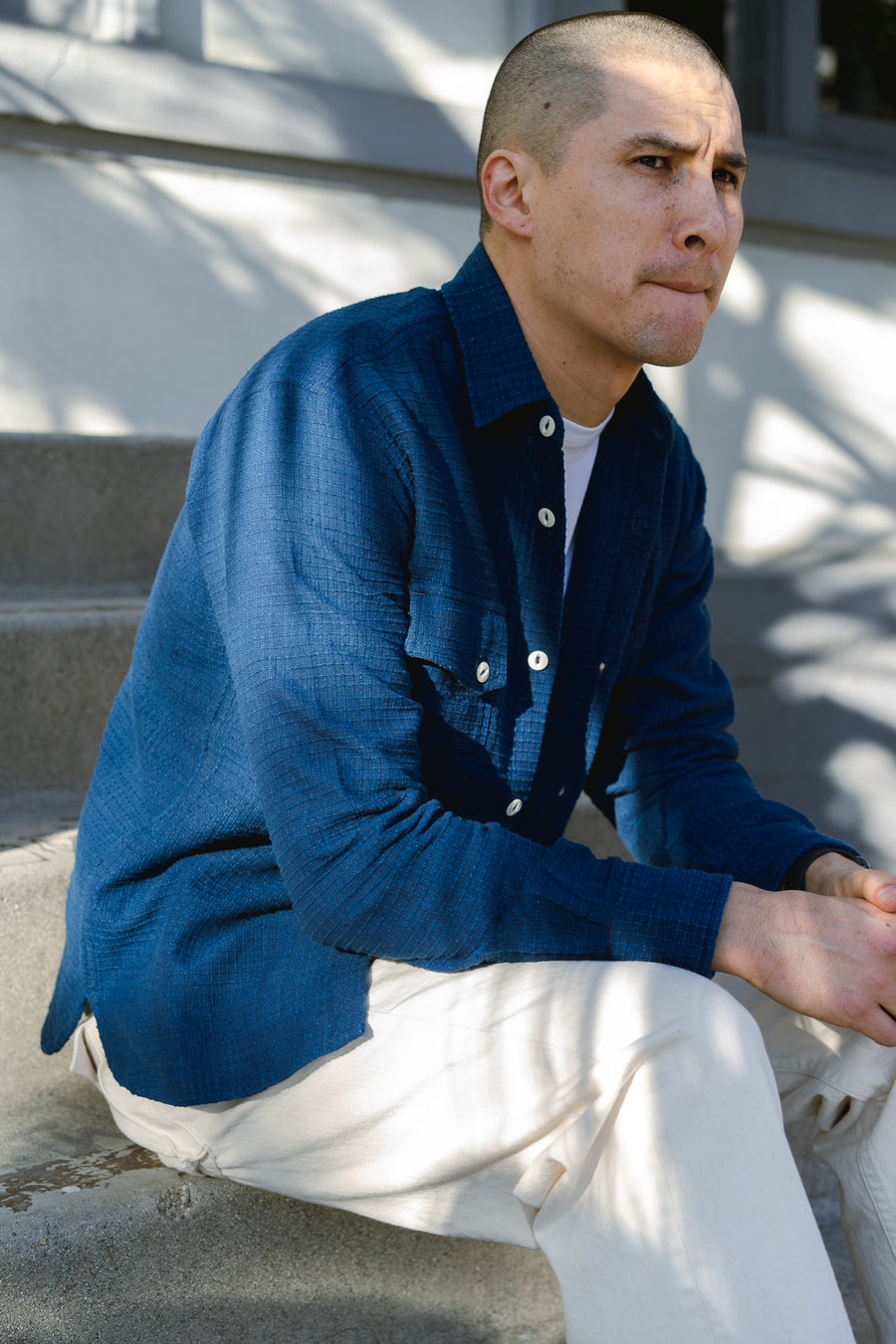 A man wears an indigo shirt and sits on some steps.