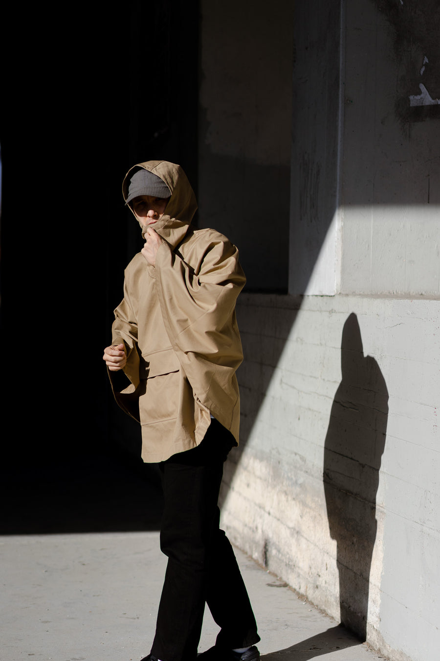 A man in a khaki poncho crosses the street.