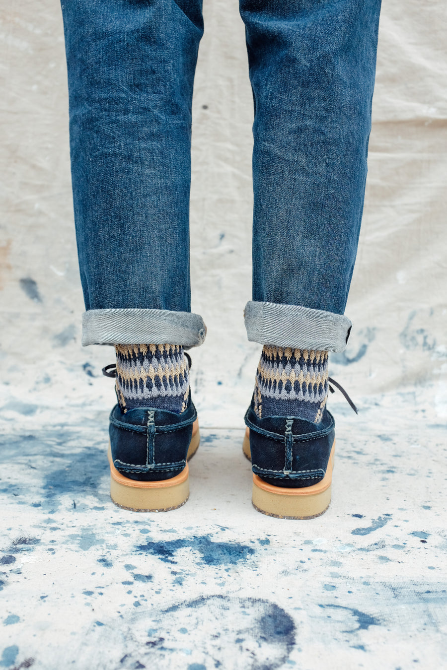 A back view of the indigo moccasins worn on feet, paired with indigo Chup socks.