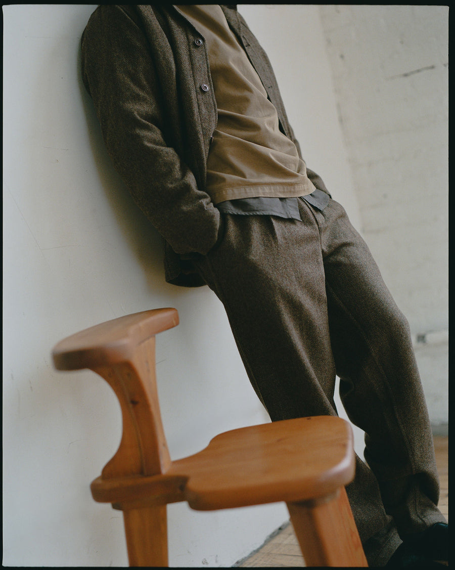 A man in earth toned clothing stands next to a chair.