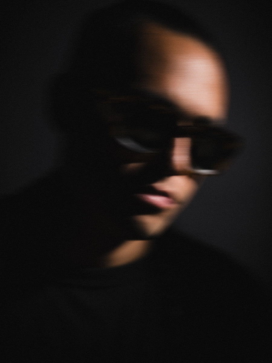A blurry image of a man in large sunglasses against a black background.