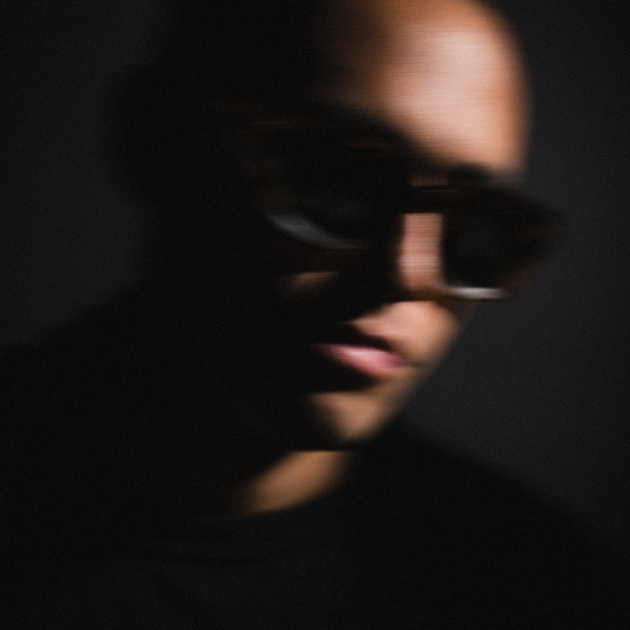 A blurry image of a man in large sunglasses against a black background.