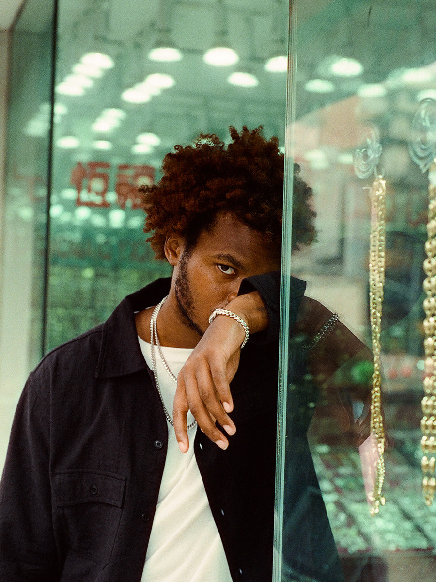 A man stands outside a jewelry store with white gold chains and bracelet on.