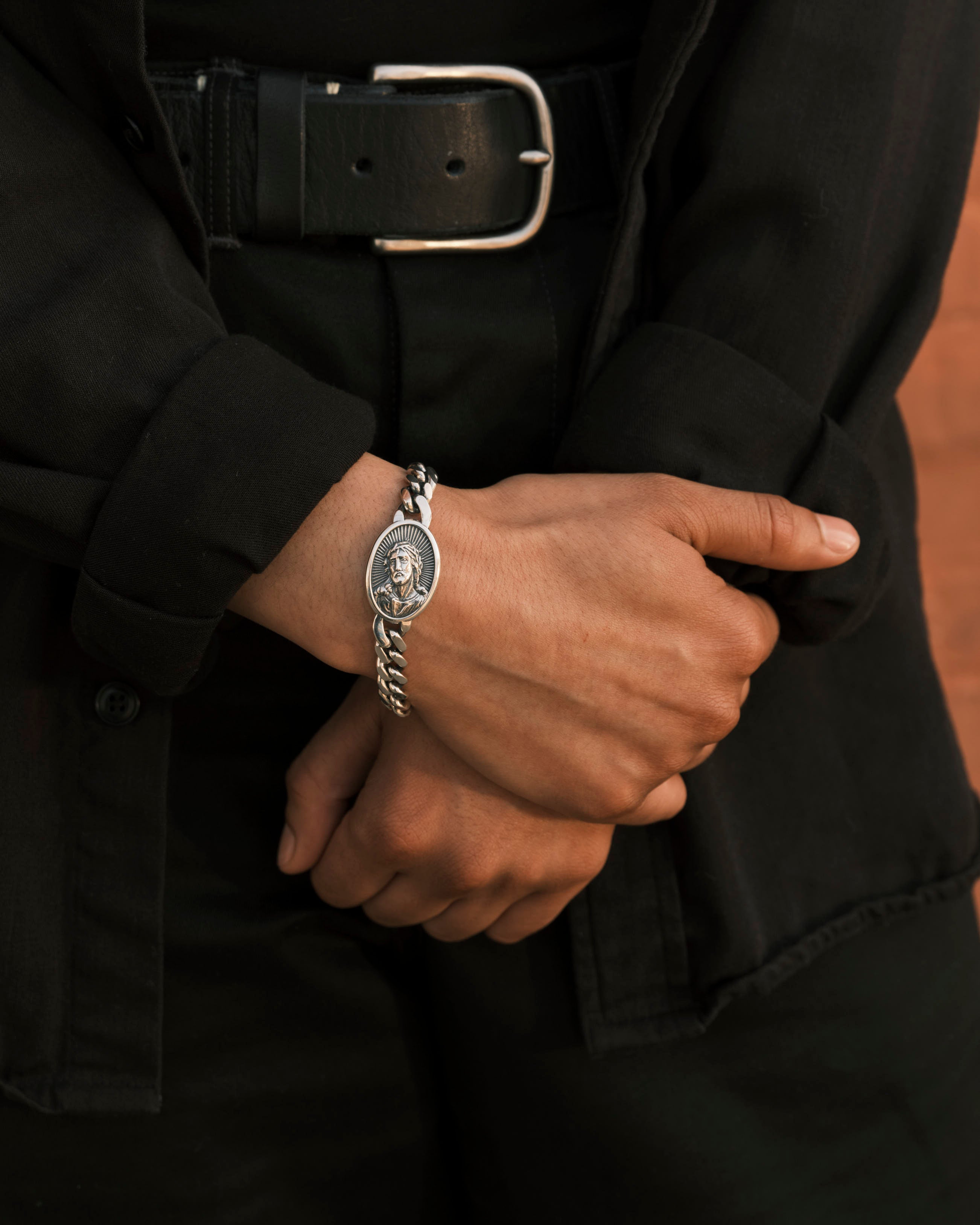A silver bracelet with a Jesus head medalliaon is worn on a wrist.