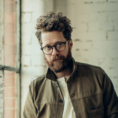 A portrait of a man in glasses and a tan jacket.