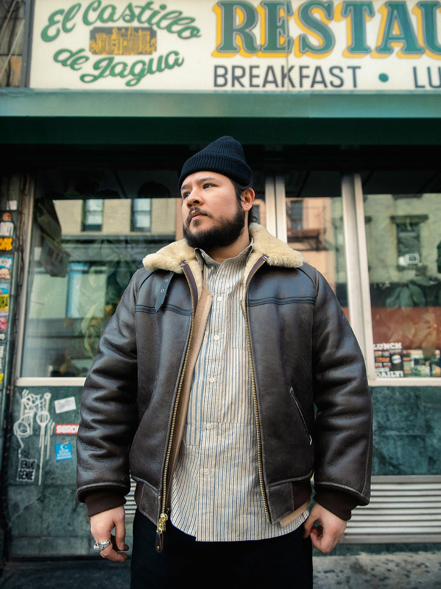 A man in a leather bomber jacket stands outside a restaurant.