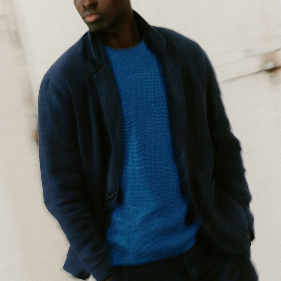 A blurry photo of a man in a navy blazer over a light blue sweater.
