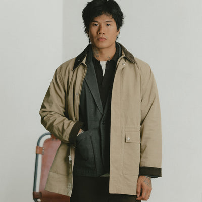 A man in a tan coat layered over a charcoal blazer with one hand in his pocket.