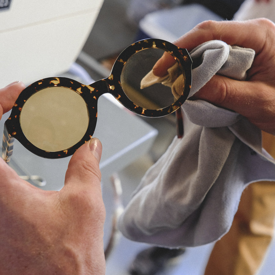 A man holds a finished pair of yellow round-lens sunglasses in his hands.