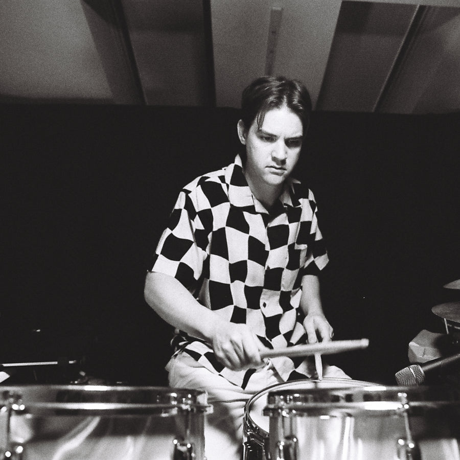 A man in a checkered shirt plays drums.