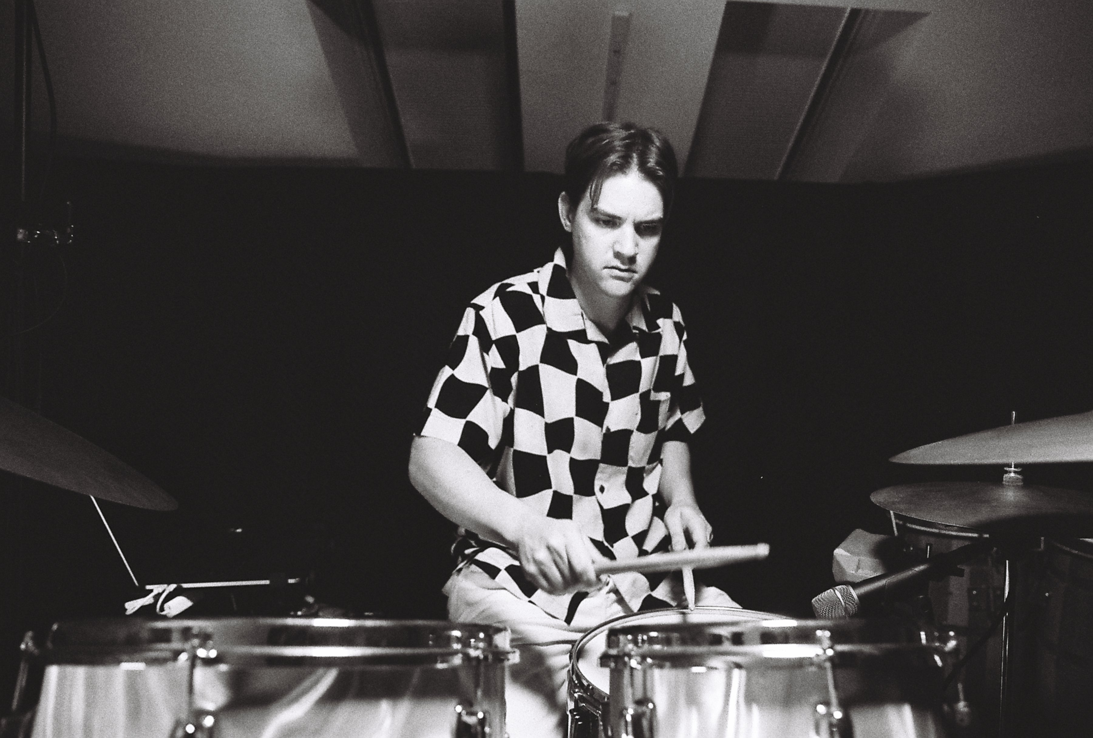 A man in a checkered shirt plays drums.