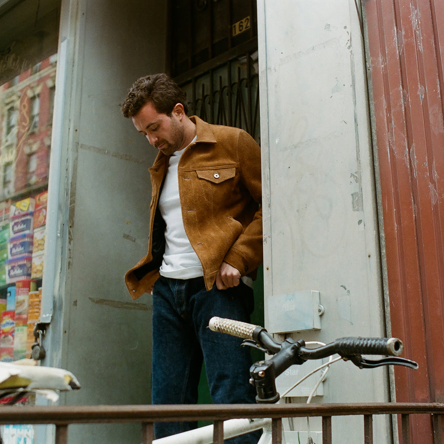 A blurry photo of someone in a tan jacket crossing a street.
