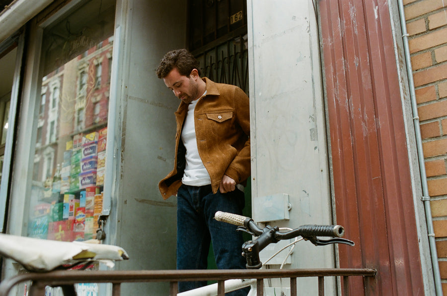 A blurry photo of someone in a tan jacket crossing a street.