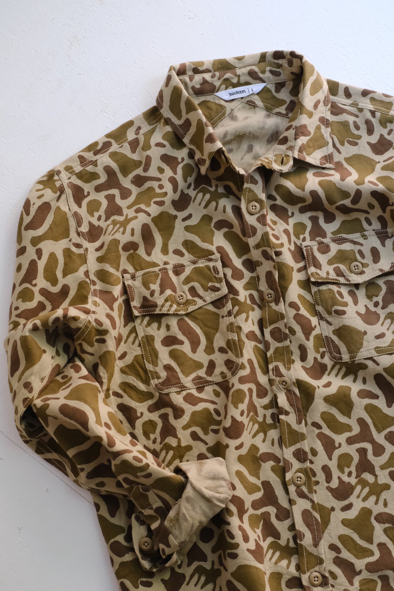 A shot of a camouflage shirt with rolled sleeves on the floor.